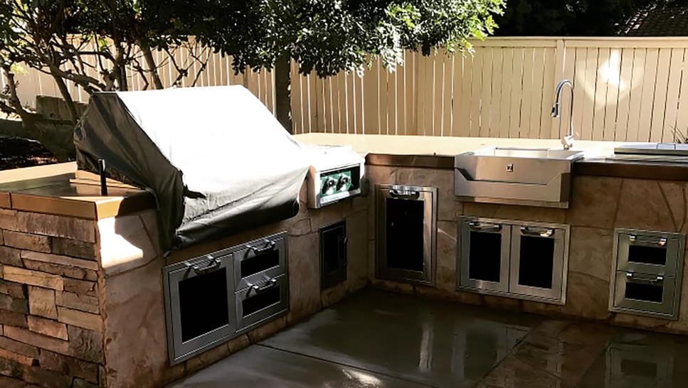 a outdoor kitchen with a grill and a white fence